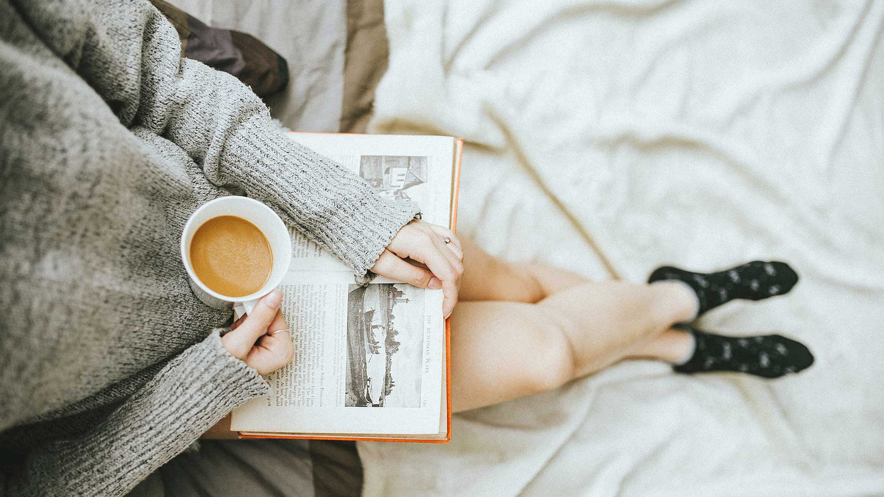 girl on be reading book with a cup of tea